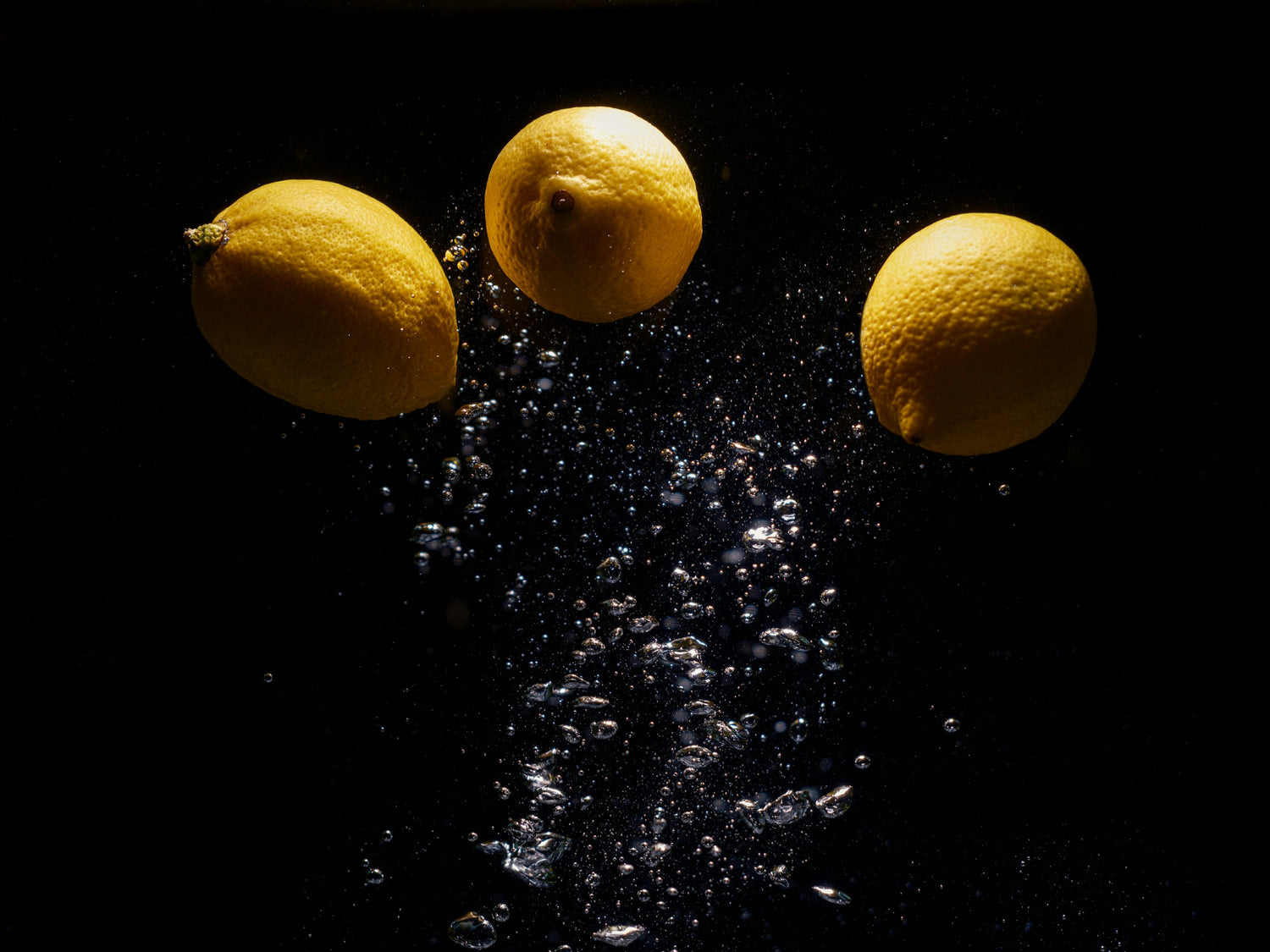 Three lemons submerged in water with rising air bubbles, dramatically lit against a black background