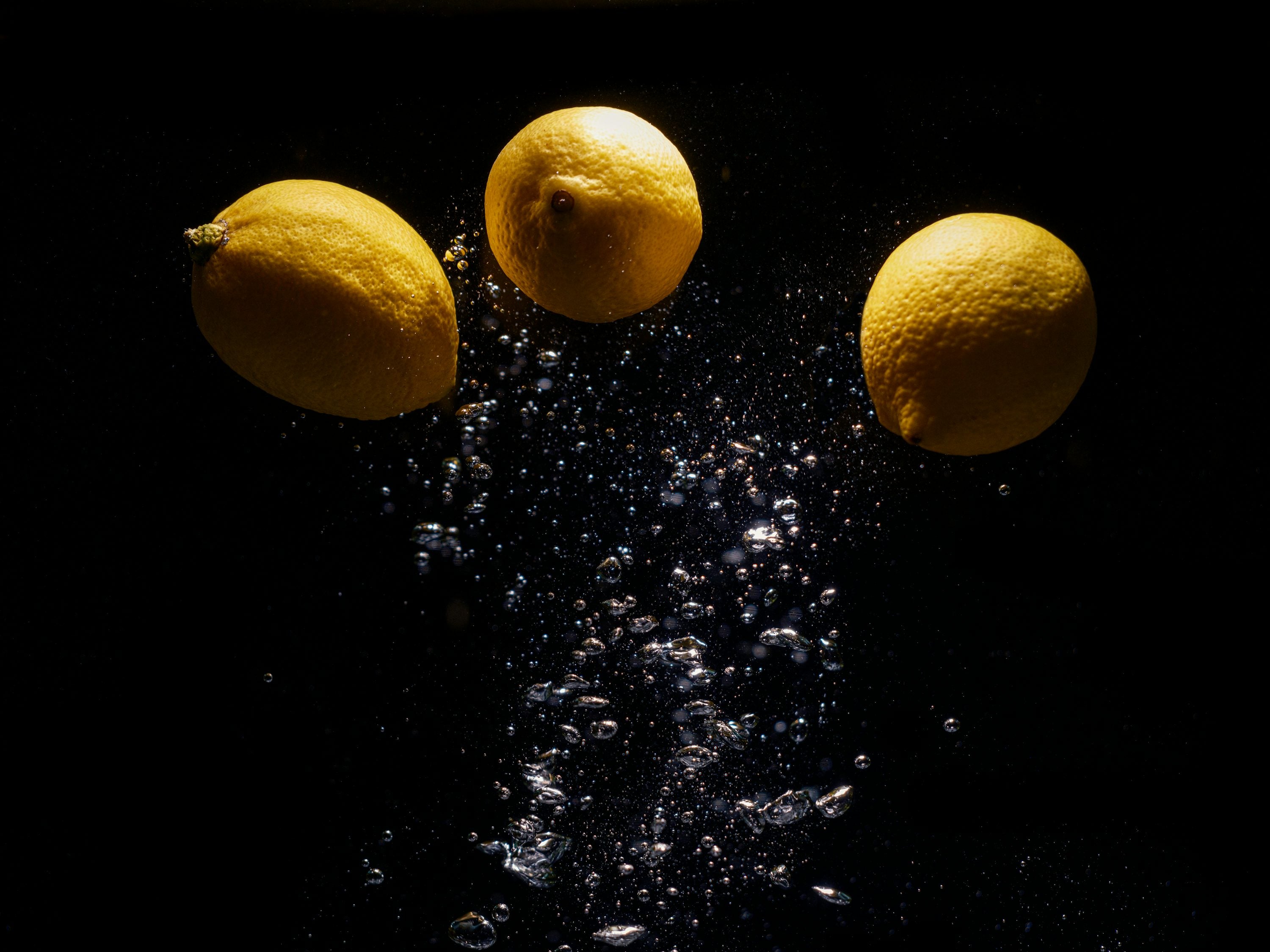 Three lemons submerged in water with rising air bubbles, dramatically lit against a black background