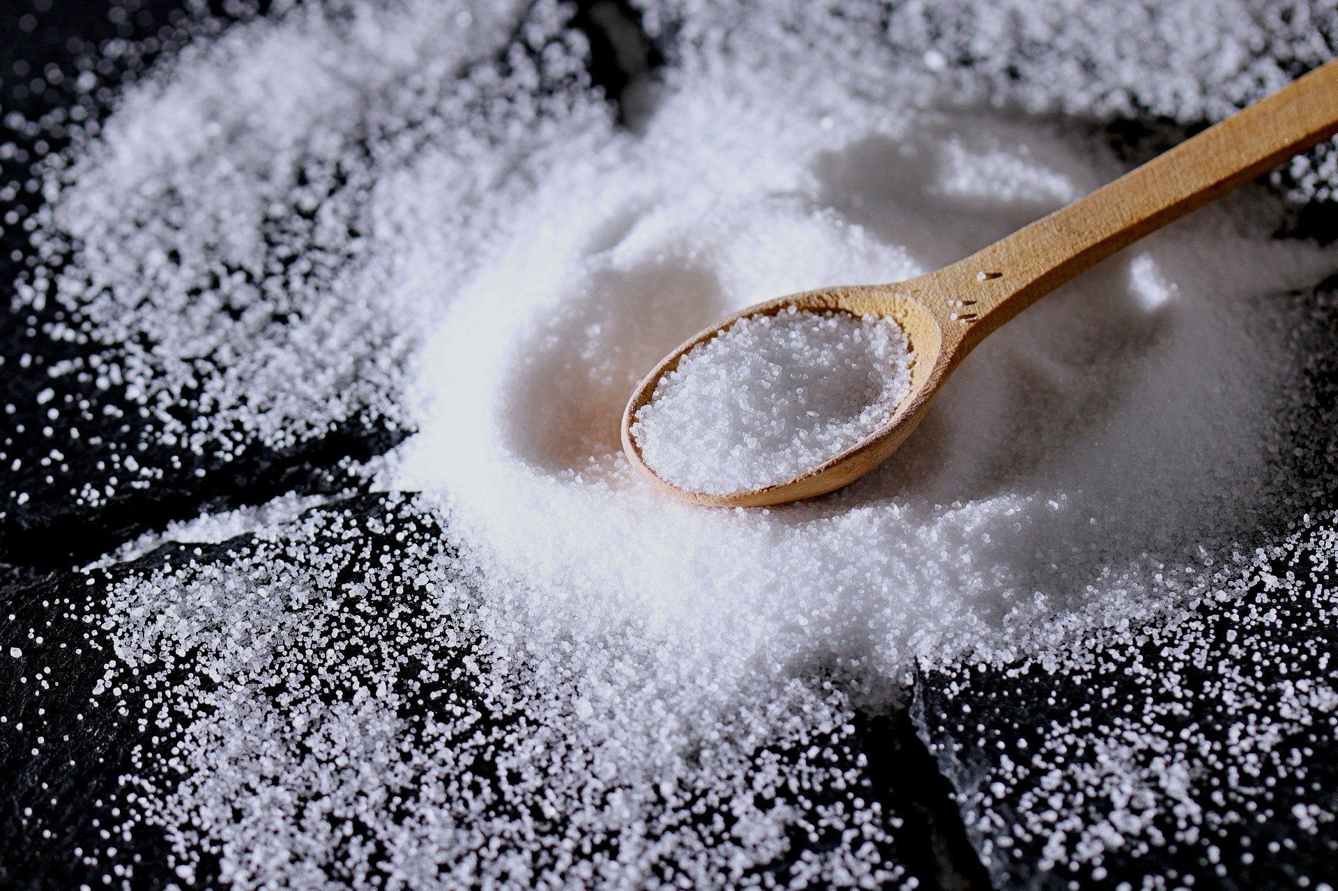 Close-up of coarse salt on a dark surface with a wooden spoon resting on a small pile